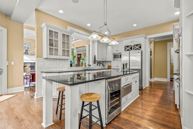 kitchen with beverage cooler, tasteful backsplash, hardwood / wood-style floors, white cabinets, and appliances with stainless steel finishes