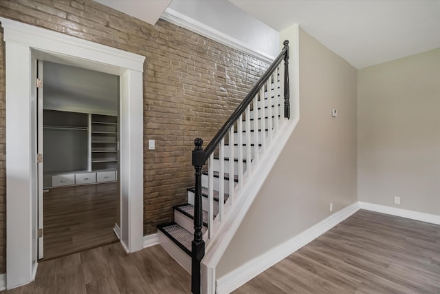 staircase featuring wood-type flooring and brick wall