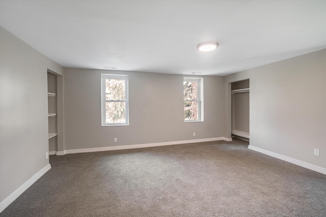 unfurnished bedroom featuring dark colored carpet and multiple windows