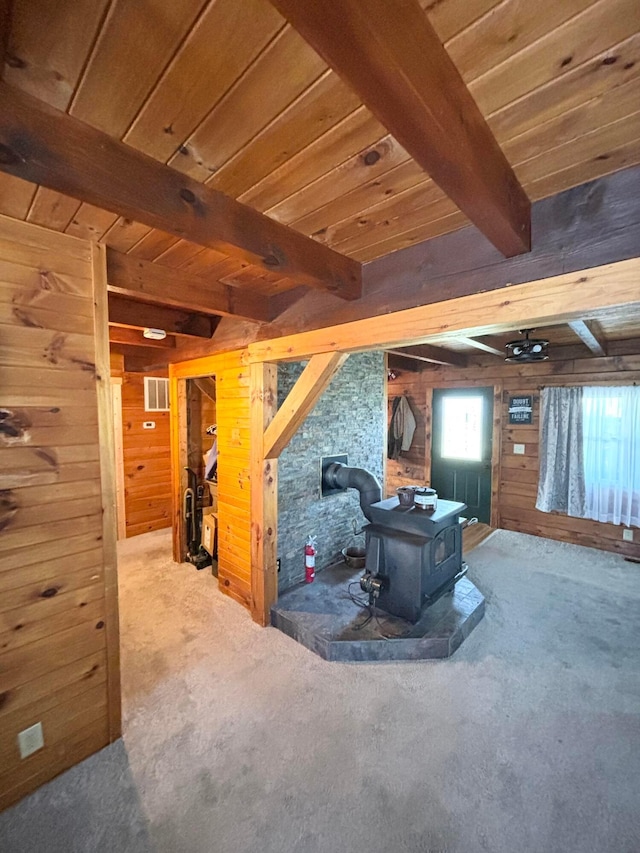 interior space with carpet, wood ceiling, beamed ceiling, a wood stove, and wood walls