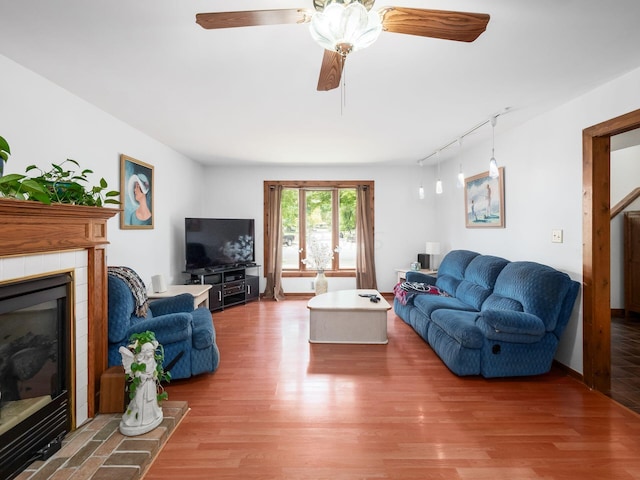 living room featuring a tiled fireplace, ceiling fan, rail lighting, and hardwood / wood-style flooring