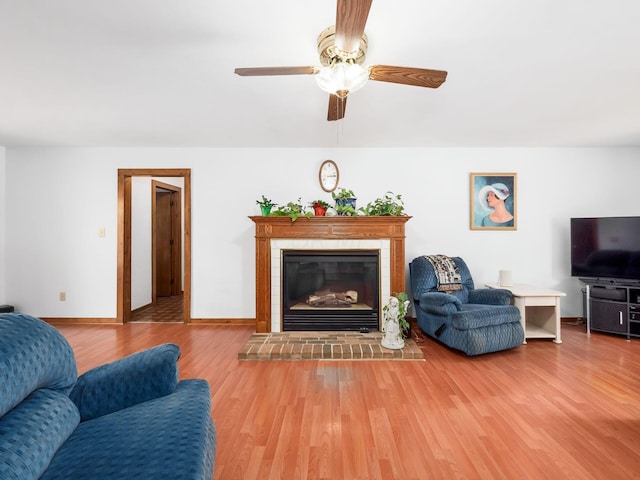 living room featuring wood-type flooring, a brick fireplace, and ceiling fan