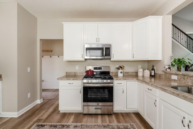 kitchen with white cabinets, light wood-type flooring, a textured ceiling, and appliances with stainless steel finishes