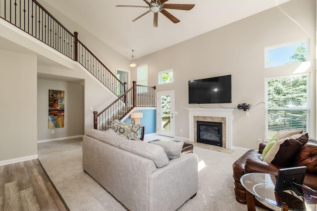 living room featuring hardwood / wood-style flooring, ceiling fan, a tile fireplace, and a high ceiling