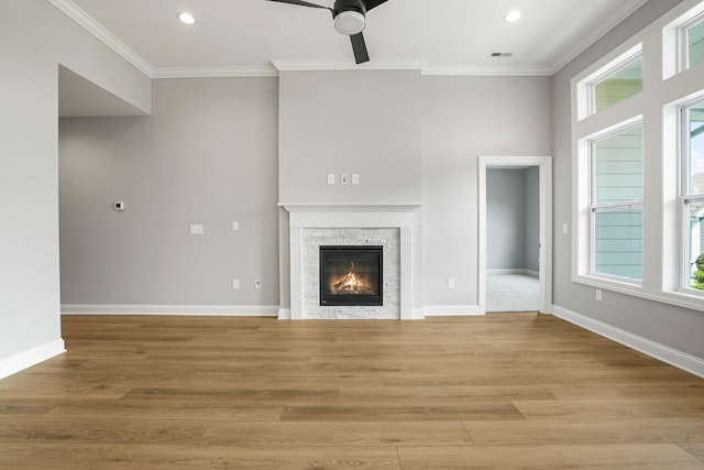 unfurnished living room with a stone fireplace, crown molding, plenty of natural light, and light wood-type flooring