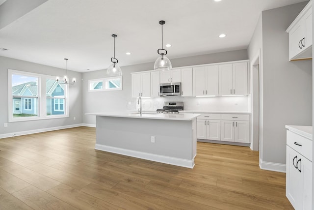 kitchen featuring pendant lighting, stainless steel appliances, light hardwood / wood-style floors, and an island with sink