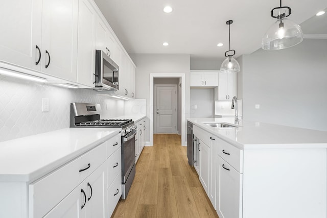 kitchen featuring white cabinetry, light hardwood / wood-style flooring, decorative light fixtures, a center island with sink, and appliances with stainless steel finishes