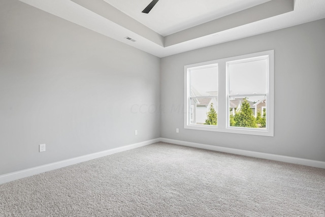 carpeted spare room with a tray ceiling and ceiling fan