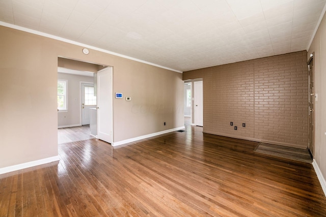 empty room featuring wood-type flooring, crown molding, and brick wall