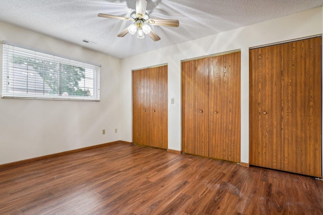 unfurnished bedroom featuring a textured ceiling, ceiling fan, dark hardwood / wood-style flooring, and two closets