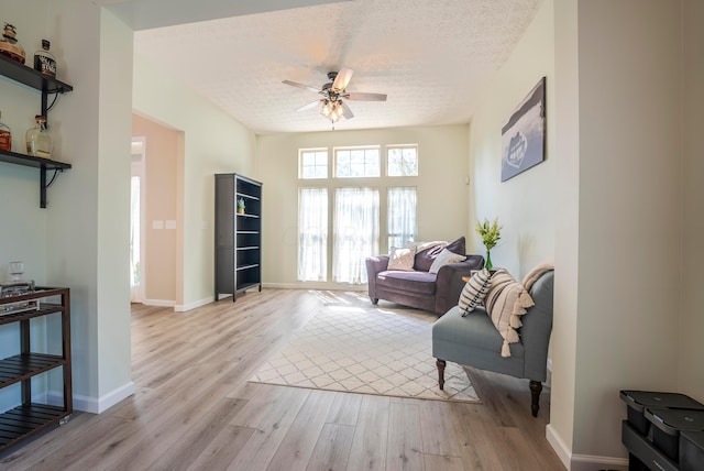 living area with ceiling fan, light hardwood / wood-style flooring, and a textured ceiling