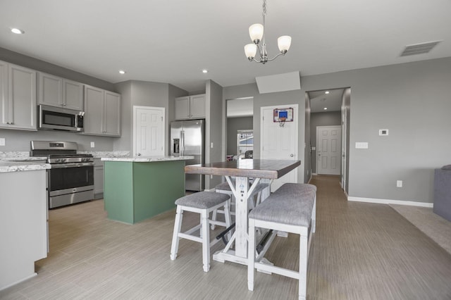 kitchen featuring appliances with stainless steel finishes, light stone counters, gray cabinetry, a chandelier, and a kitchen island