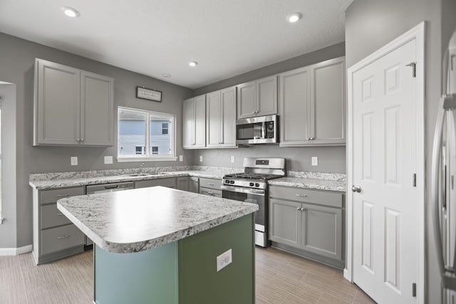 kitchen featuring appliances with stainless steel finishes, sink, gray cabinets, a kitchen island, and a breakfast bar area