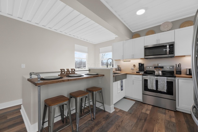 kitchen featuring stainless steel appliances, white cabinetry, a kitchen bar, wood counters, and dark hardwood / wood-style flooring