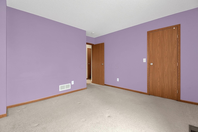 spare room featuring light colored carpet and a textured ceiling