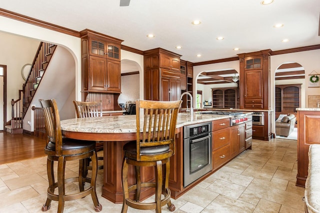 kitchen featuring appliances with stainless steel finishes, a kitchen breakfast bar, light stone counters, ornamental molding, and a kitchen island with sink