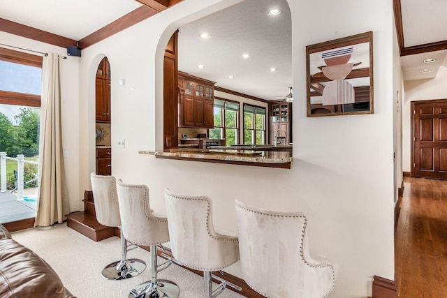 bar with ceiling fan, light stone countertops, wood-type flooring, and ornamental molding