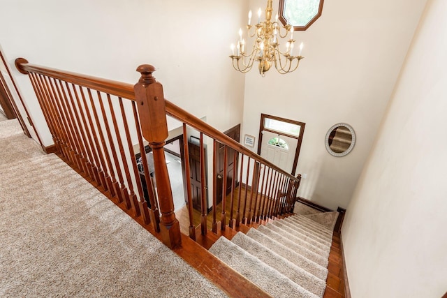 staircase with a towering ceiling, a chandelier, and wood-type flooring