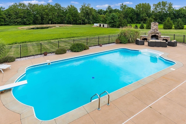 view of swimming pool featuring a lawn, an outdoor stone fireplace, a diving board, and a patio area