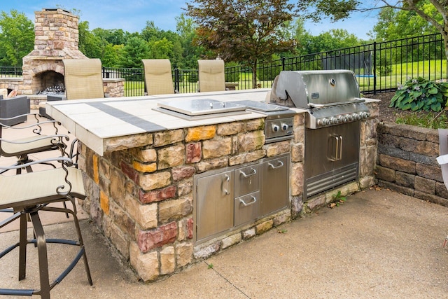 view of patio with area for grilling, a grill, and an outdoor stone fireplace