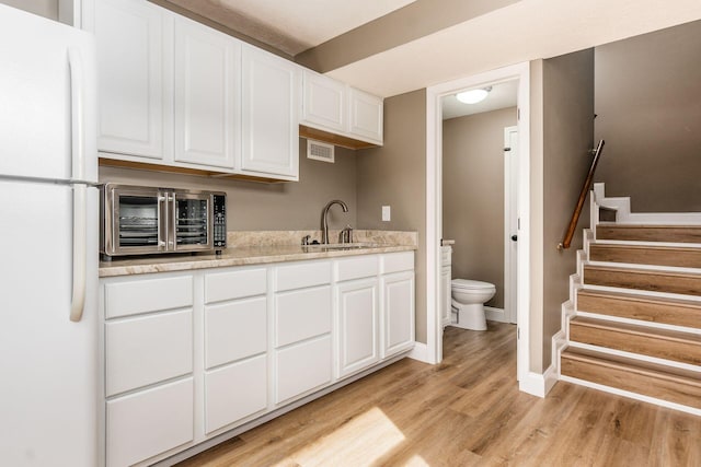 kitchen with sink, light stone countertops, light wood-type flooring, white fridge, and white cabinetry