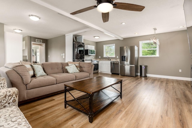 living room with stacked washing maching and dryer, ceiling fan, sink, beamed ceiling, and light hardwood / wood-style floors