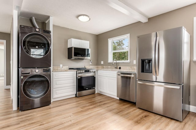 kitchen with beam ceiling, white cabinetry, stacked washer / dryer, light hardwood / wood-style floors, and appliances with stainless steel finishes