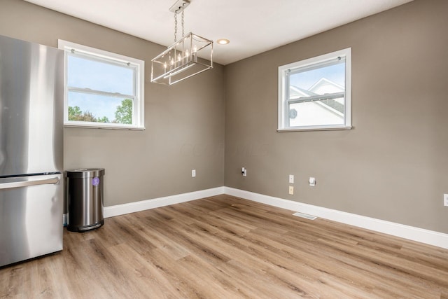 unfurnished dining area with a chandelier and light wood-type flooring