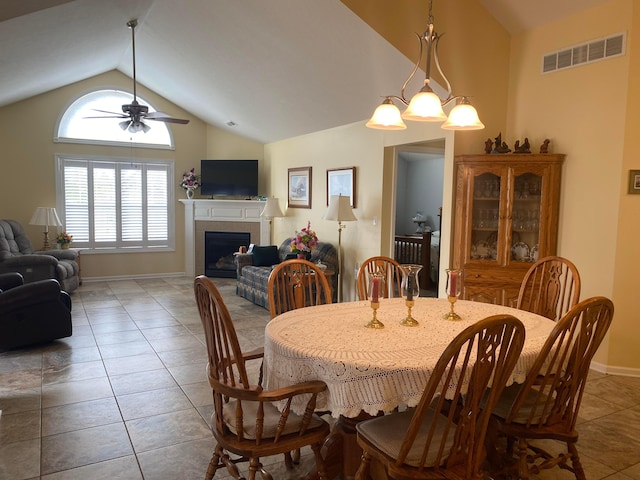 dining space featuring vaulted ceiling, a tile fireplace, light tile patterned flooring, and ceiling fan with notable chandelier