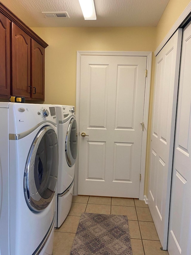 laundry area with washer and clothes dryer, cabinets, light tile patterned floors, and a textured ceiling