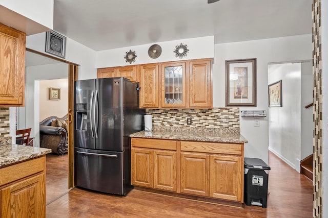 kitchen with stainless steel fridge, backsplash, light stone counters, and hardwood / wood-style floors