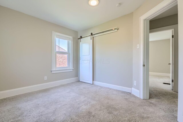 unfurnished bedroom featuring a barn door and light colored carpet