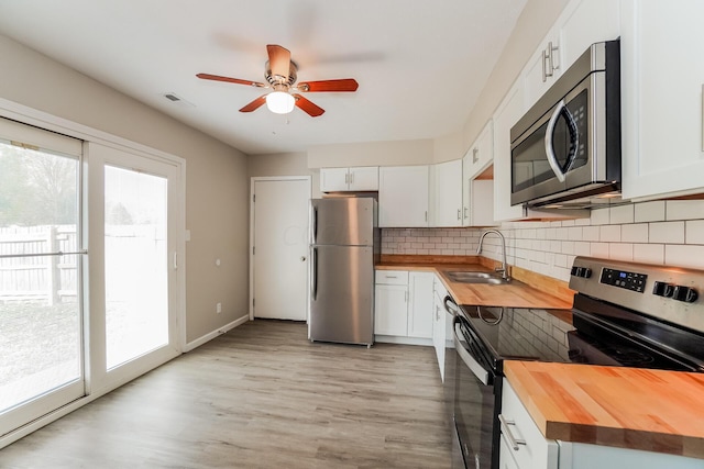 kitchen with wood counters, stainless steel appliances, white cabinetry, and plenty of natural light