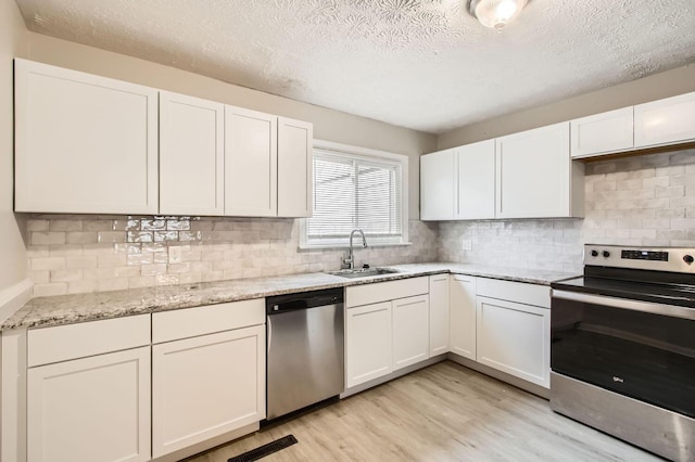 kitchen featuring sink, light hardwood / wood-style floors, decorative backsplash, white cabinets, and appliances with stainless steel finishes