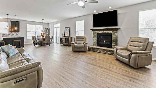 living room with hardwood / wood-style flooring, a stone fireplace, and ceiling fan