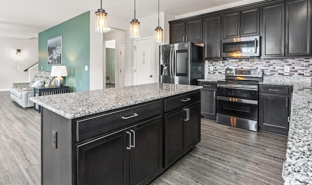 kitchen with wood-type flooring, stainless steel appliances, a kitchen island, and hanging light fixtures