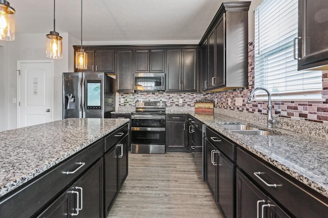 kitchen featuring sink, stainless steel appliances, light hardwood / wood-style flooring, pendant lighting, and dark brown cabinets