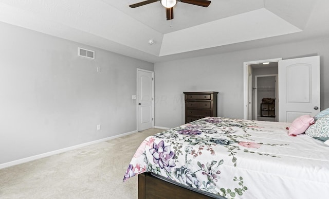 bedroom featuring ceiling fan, light carpet, a tray ceiling, and a closet