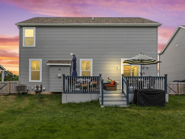 back house at dusk with central AC, a lawn, and a wooden deck