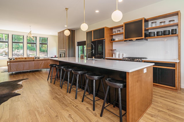 kitchen with pendant lighting, light wood-type flooring, stainless steel range oven, and an island with sink