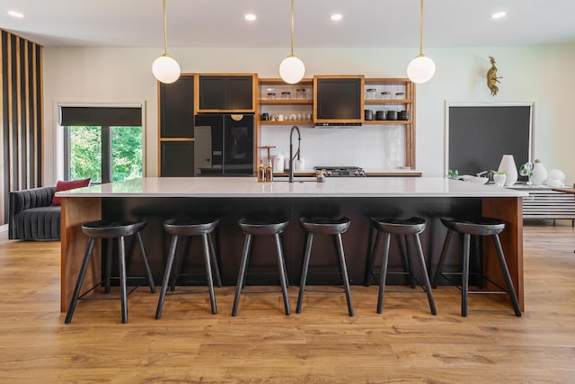 kitchen with a kitchen bar, black fridge, light hardwood / wood-style floors, and decorative light fixtures