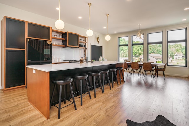 kitchen with pendant lighting, a breakfast bar, sink, an island with sink, and light hardwood / wood-style floors