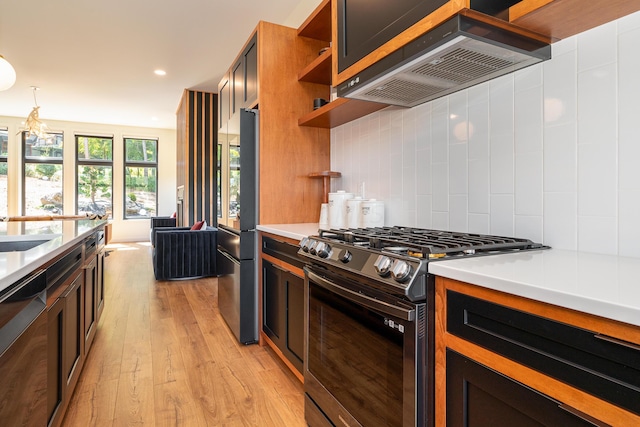 kitchen with wall chimney exhaust hood, black dishwasher, gas range oven, pendant lighting, and light wood-type flooring