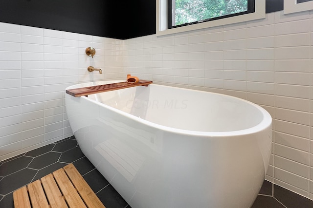 bathroom featuring a washtub, tile patterned flooring, and tile walls