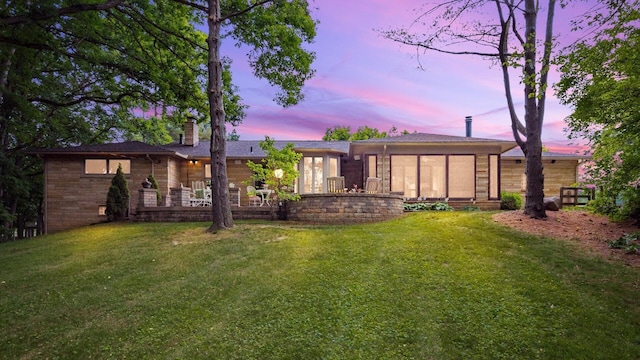 back house at dusk featuring a lawn and a sunroom