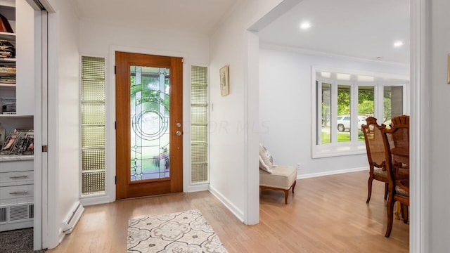 foyer featuring baseboard heating, light hardwood / wood-style flooring, a healthy amount of sunlight, and ornamental molding