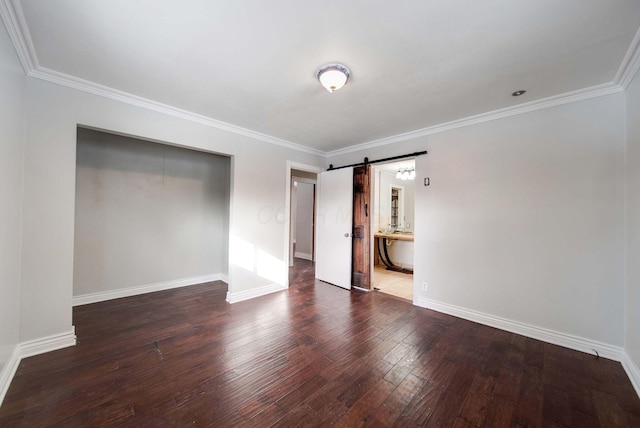 unfurnished bedroom featuring crown molding, ensuite bathroom, a barn door, dark hardwood / wood-style flooring, and a closet