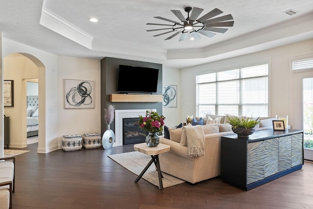 living room with a brick fireplace, dark hardwood / wood-style flooring, a raised ceiling, and crown molding