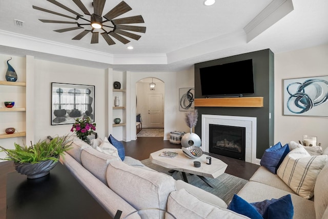 living room featuring a tray ceiling, ceiling fan, crown molding, and wood-type flooring