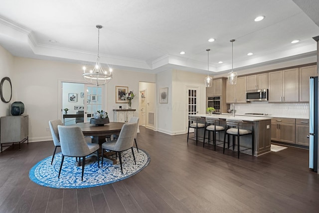 dining room with ornamental molding, dark hardwood / wood-style floors, an inviting chandelier, and a tray ceiling